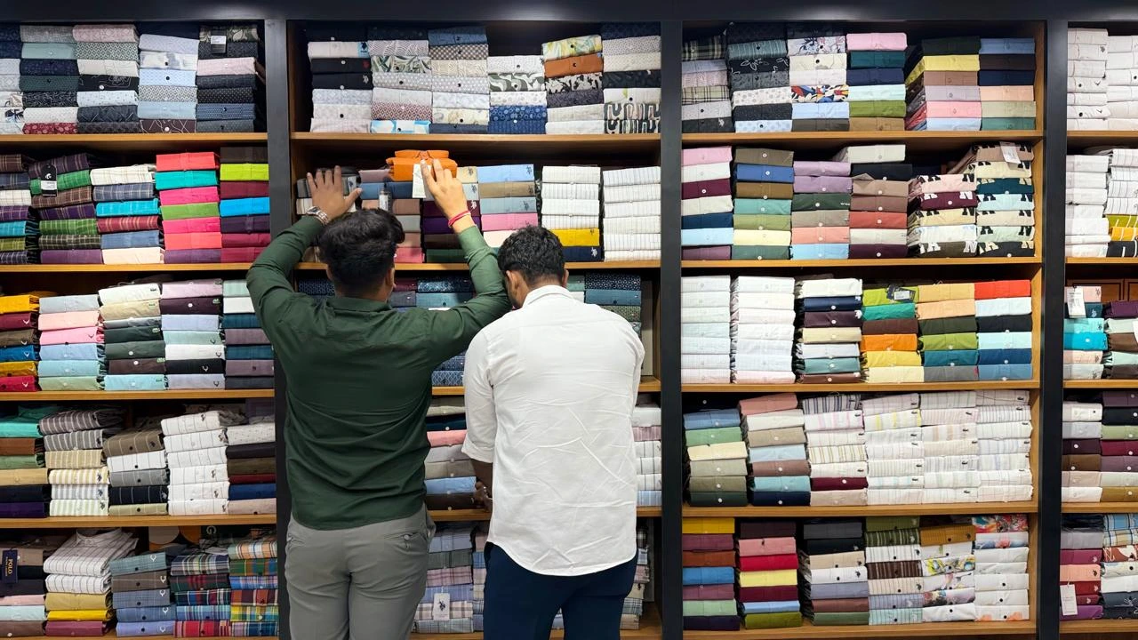 Two team members selecting folded shirts from stocked shelves in the Maaax store