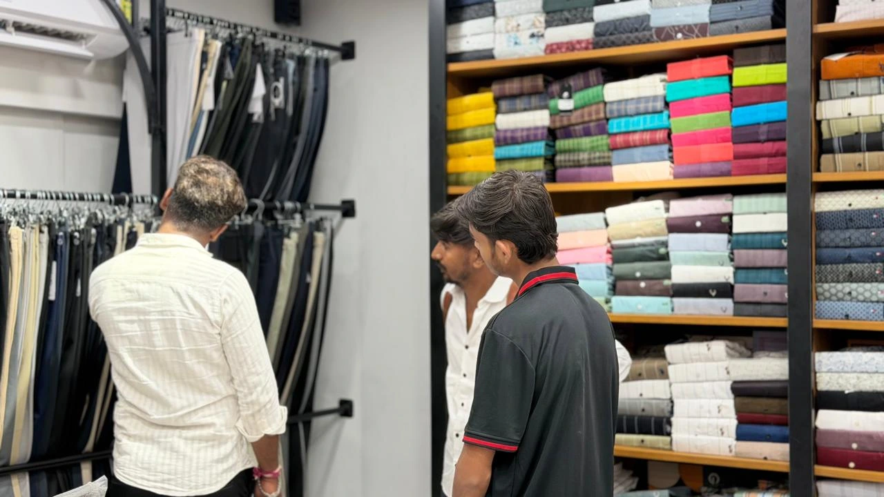 A customer and store associates reviewing garments beside trouser racks and folded shirt shelves