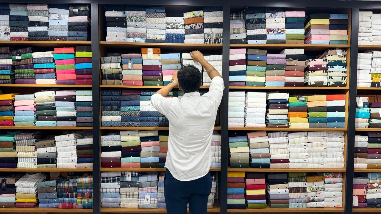 A team member arranging folded shirts on the shelves at Maaax