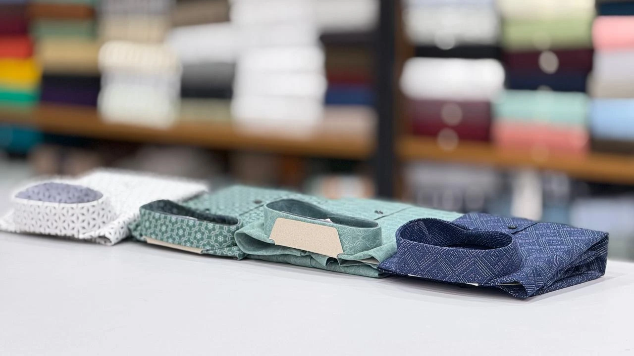 Folded patterned shirts in white, sage green and navy displayed on a store counter.