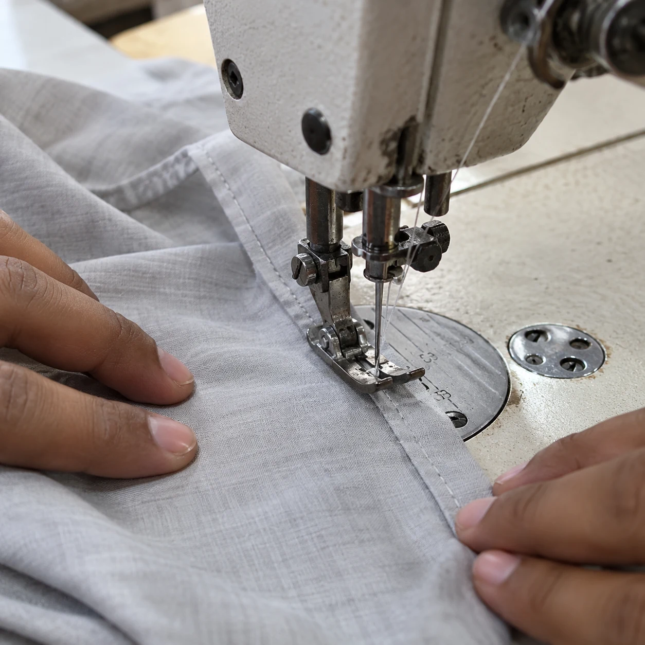 AI-generated illustrative image: Apparel worker sewing gray fabric at an industrial machine