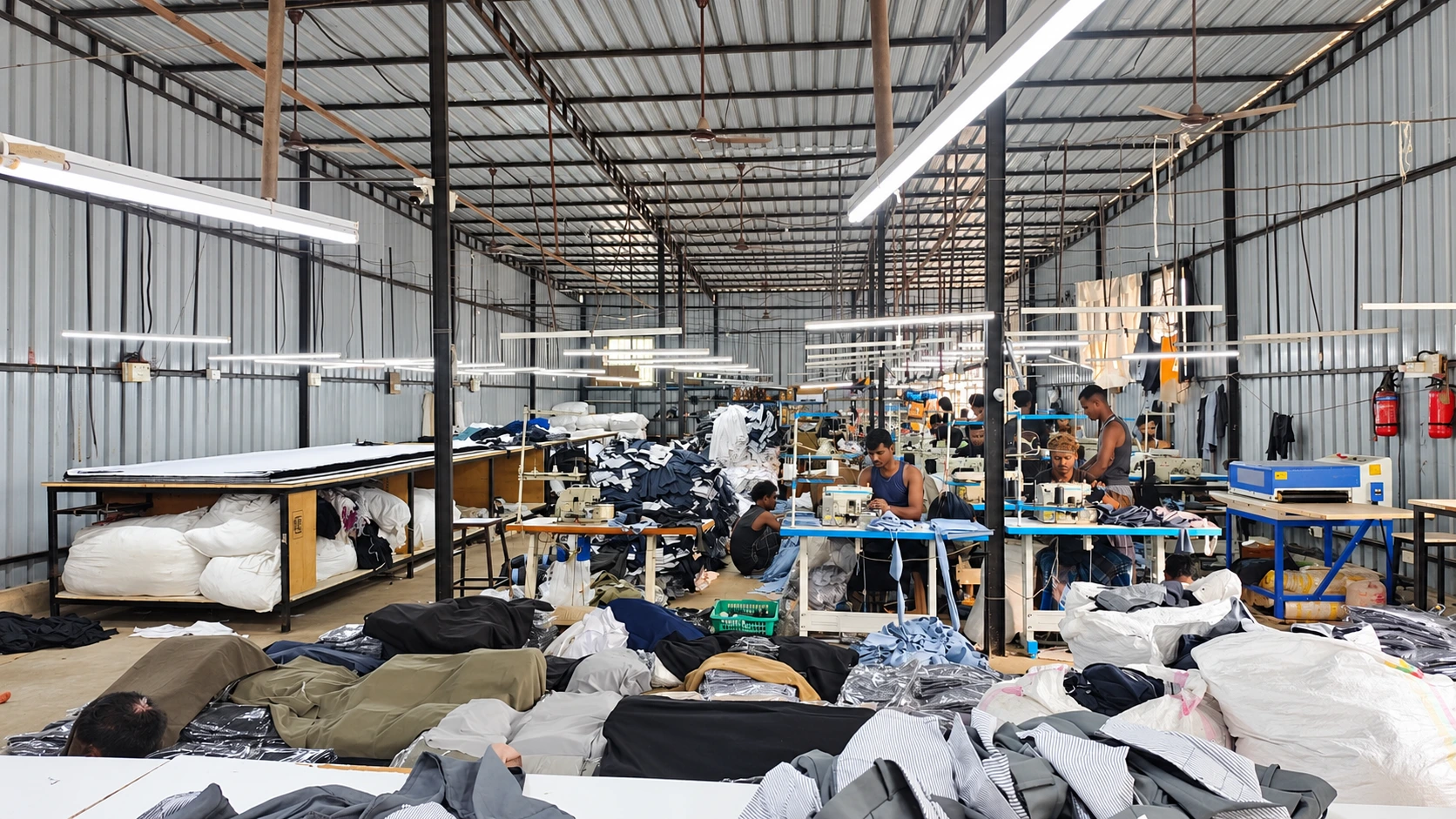 Retouched photograph of the Shivraya sewing floor with industrial machines, fabric and team members at work